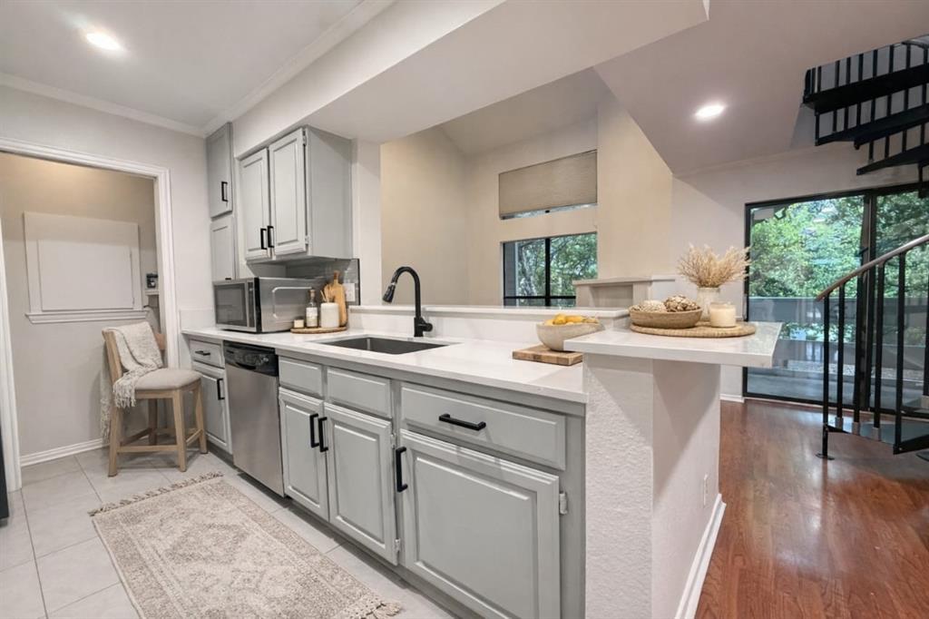 5840 Spring Valley Road, Unit 602 Dallas, TX 75254 - Photo 4 of 19 Modern kitchen featuring light gray cabinetry with black hardware, white countertops, a stainless steel dishwasher, and a black sink with a matte black faucet