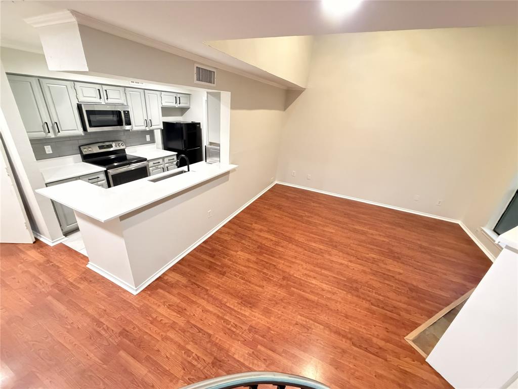 5840 Spring Valley Road, Unit 602 Dallas, TX 75254 - Photo 5 of 19 Kitchen and living area featuring wood-finish flooring, white cabinetry, a breakfast bar with white countertops, stainless steel appliances, and a black sink with a black faucet