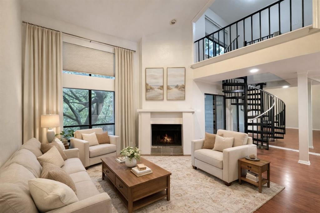 5840 Spring Valley Road, Unit 602 Dallas, TX 75254 - Photo 8 of 19 Two-story living area featuring a prominent spiral staircase, a fireplace with a white mantel, large windows with exterior views, wood-finish flooring, and a second-story interior balcony with black metal railings