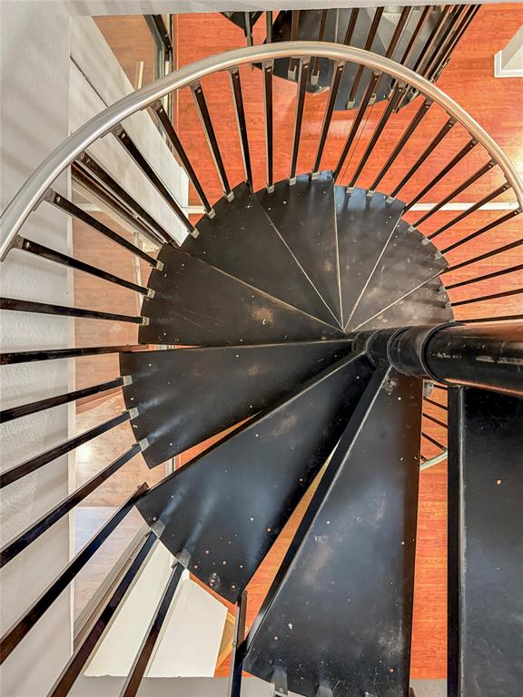 5840 Spring Valley Road, Unit 602 Dallas, TX 75254 - Photo 9 of 19 Black spiral staircase with a brushed metal handrail and balusters, set against wood-finish flooring