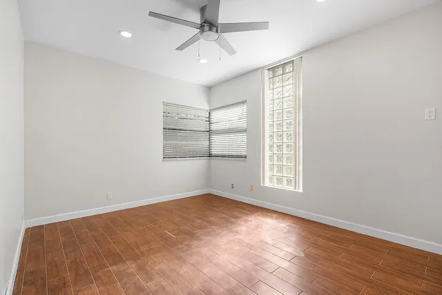 an empty room with wooden floor chandelier fan and windows