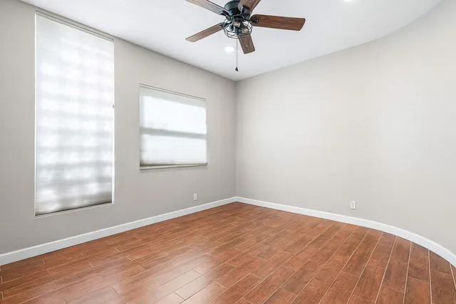 an empty room with wooden floor windows and fan