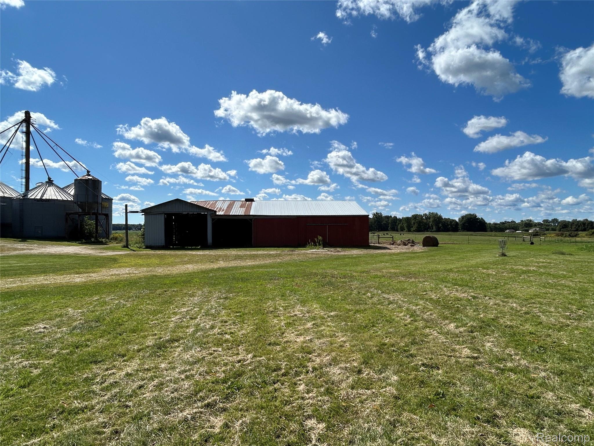16465 Almont Road Allenton, MI 48002 - Photo 4 of 35 Expansive grassy field with a red barn, an attached utility shed, and multiple grain silos