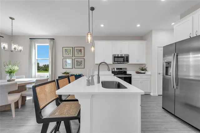 a kitchen with stainless steel appliances granite countertop a sink a stove a refrigerator and a dining table with wooden floor