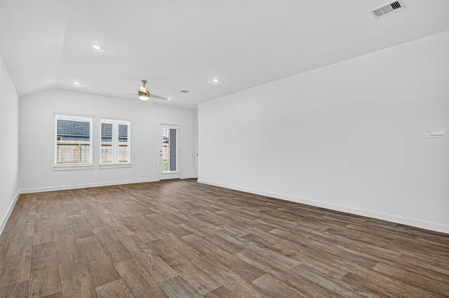a view of an empty room with wooden floor and windows