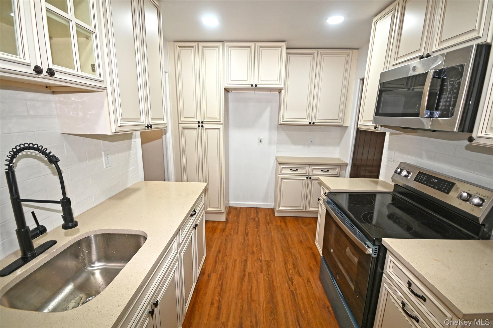 112-13 178th Street Queens, NY 11433 - Photo 12 of 28 Kitchen featuring tasteful backsplash, stainless steel appliances, dark wood-style floors, glass insert cabinets, and recessed lighting
