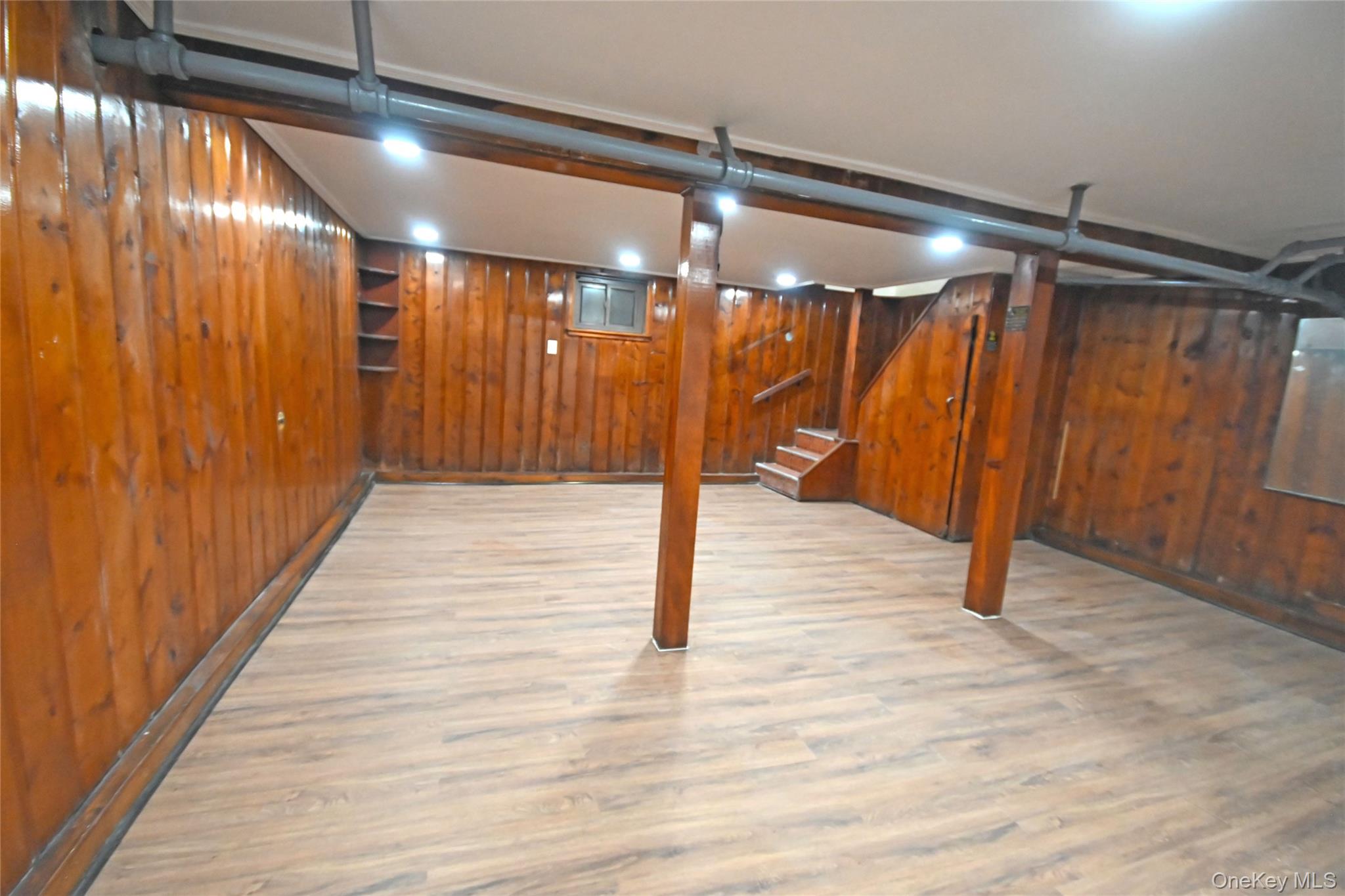 112-13 178th Street Queens, NY 11433 - Photo 23 of 28 Finished below grade area featuring a baseboard radiator, light wood-style flooring, stairs, and wooden walls