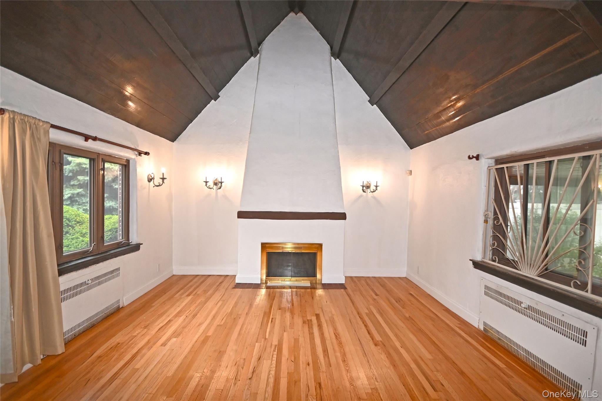 112-13 178th Street Queens, NY 11433 - Photo 4 of 28 Unfurnished living room featuring radiator, light wood-type flooring, a large fireplace, high vaulted ceiling, and wood ceiling