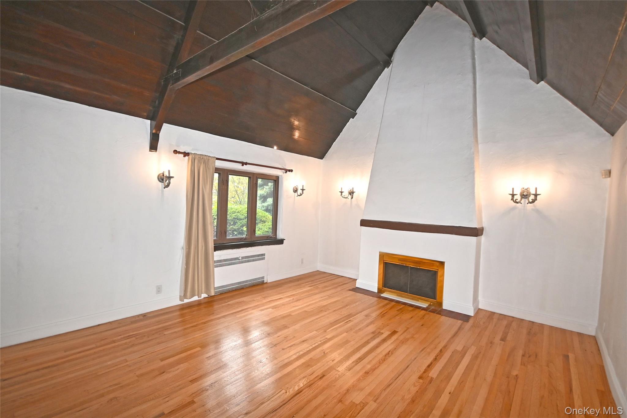 112-13 178th Street Queens, NY 11433 - Photo 5 of 28 Unfurnished living room with light wood-type flooring, a fireplace with flush hearth, beamed ceiling, radiator heating unit, and high vaulted ceiling
