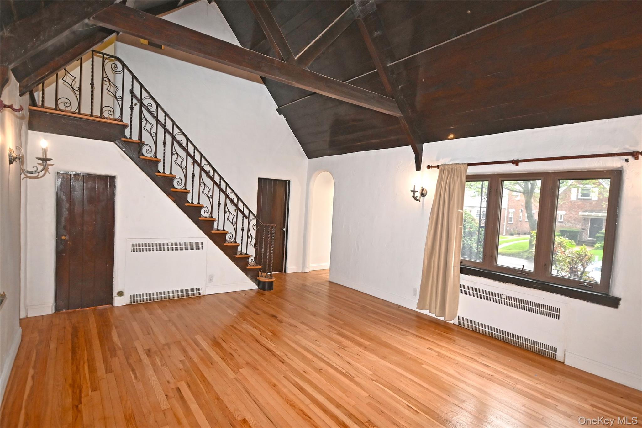 112-13 178th Street Queens, NY 11433 - Photo 6 of 28 Unfurnished living room featuring radiator, high vaulted ceiling, light wood-type flooring, arched walkways, and stairway