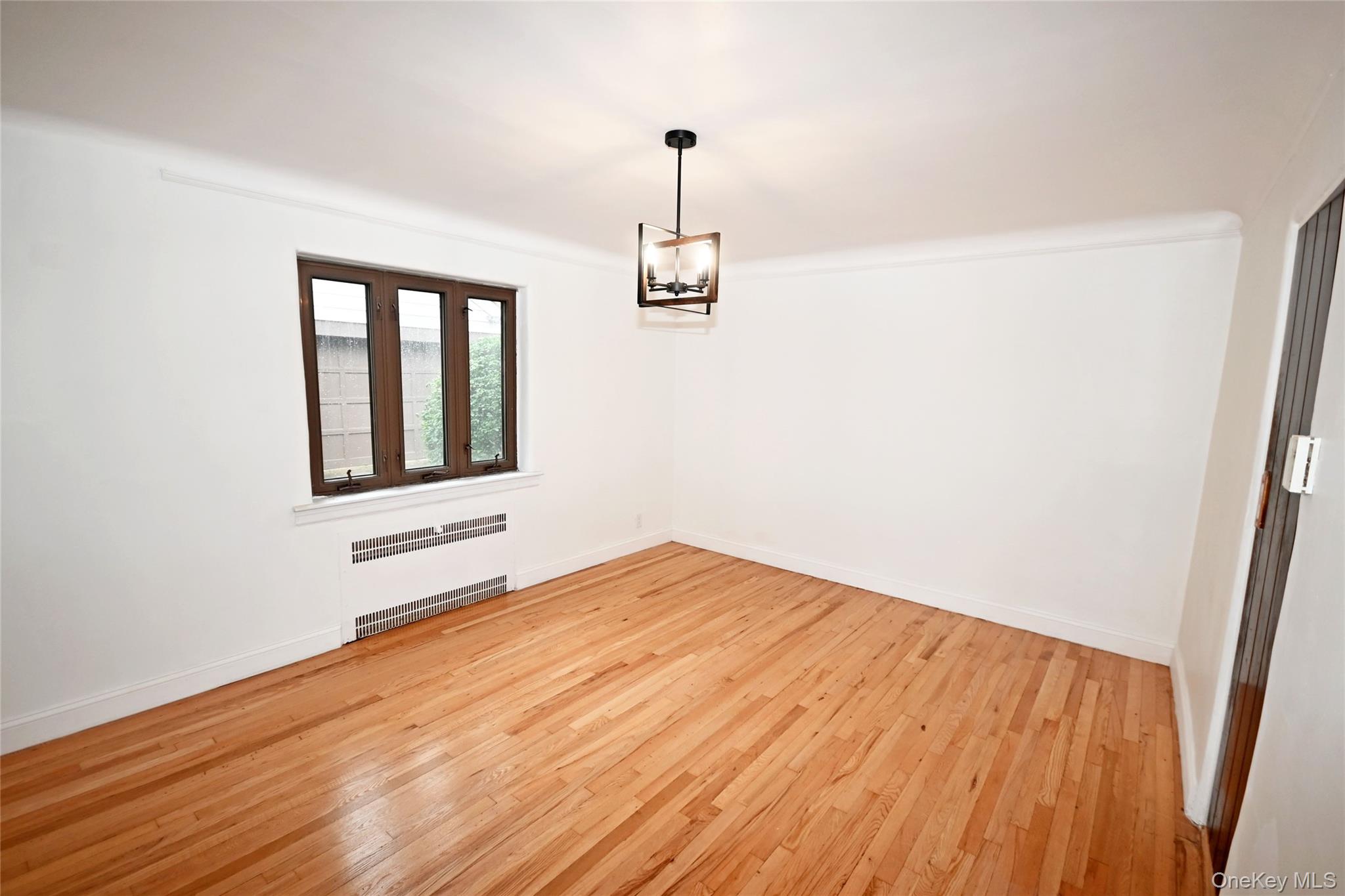 112-13 178th Street Queens, NY 11433 - Photo 8 of 28 Empty room featuring radiator heating unit, light wood-style flooring, and a chandelier
