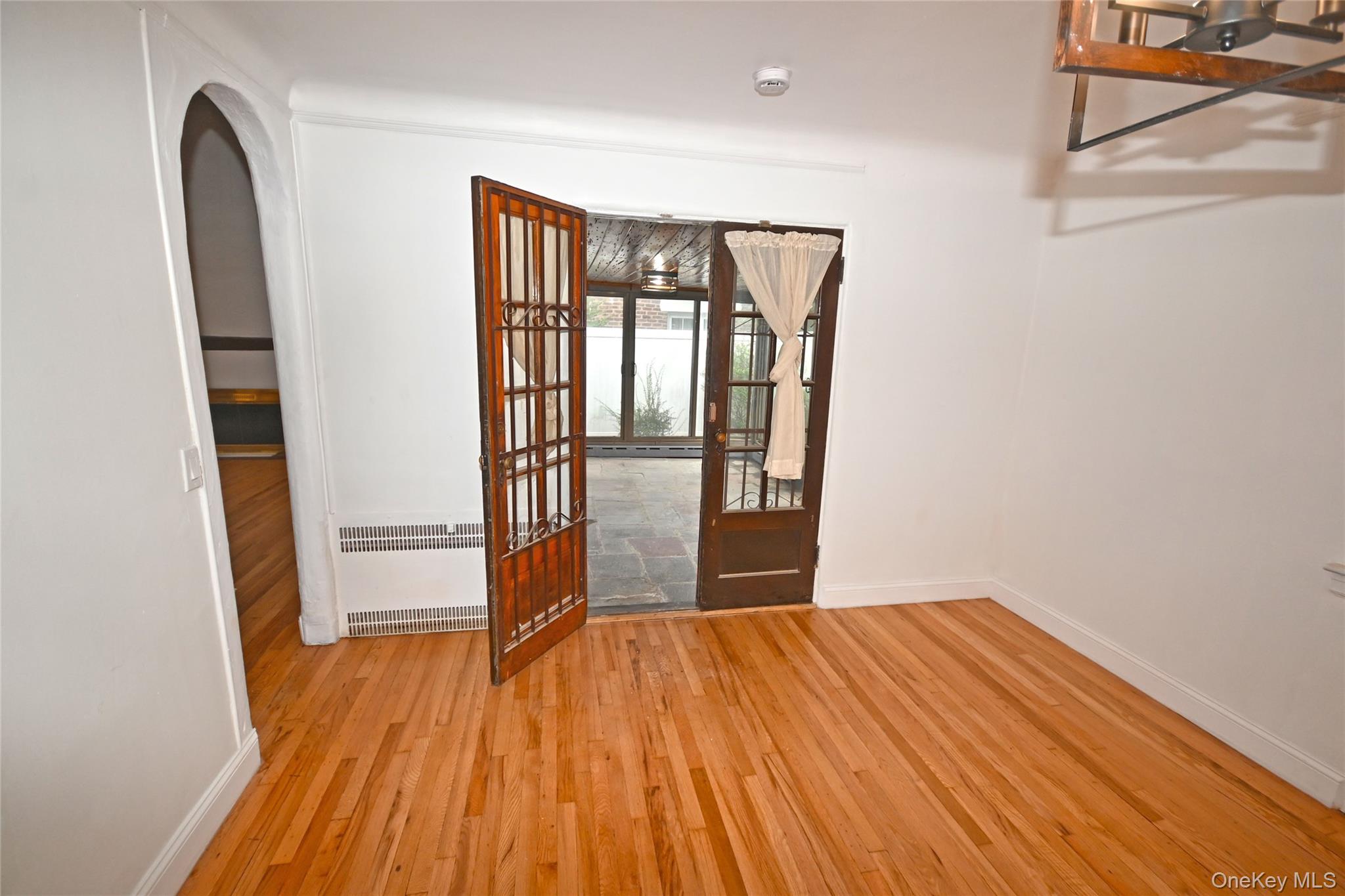112-13 178th Street Queens, NY 11433 - Photo 9 of 28 Empty room with light wood-style flooring, radiator, arched walkways, and french doors