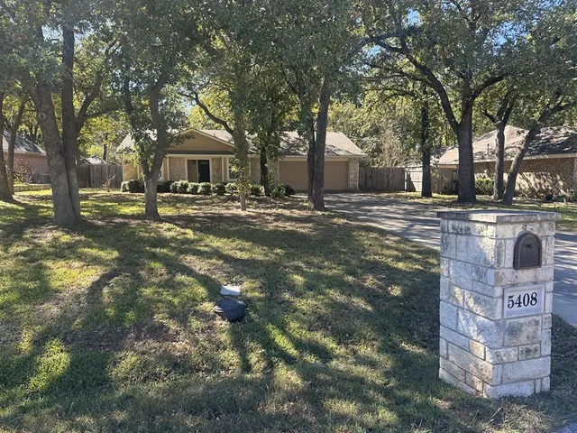 a front view of a house with a yard and large trees