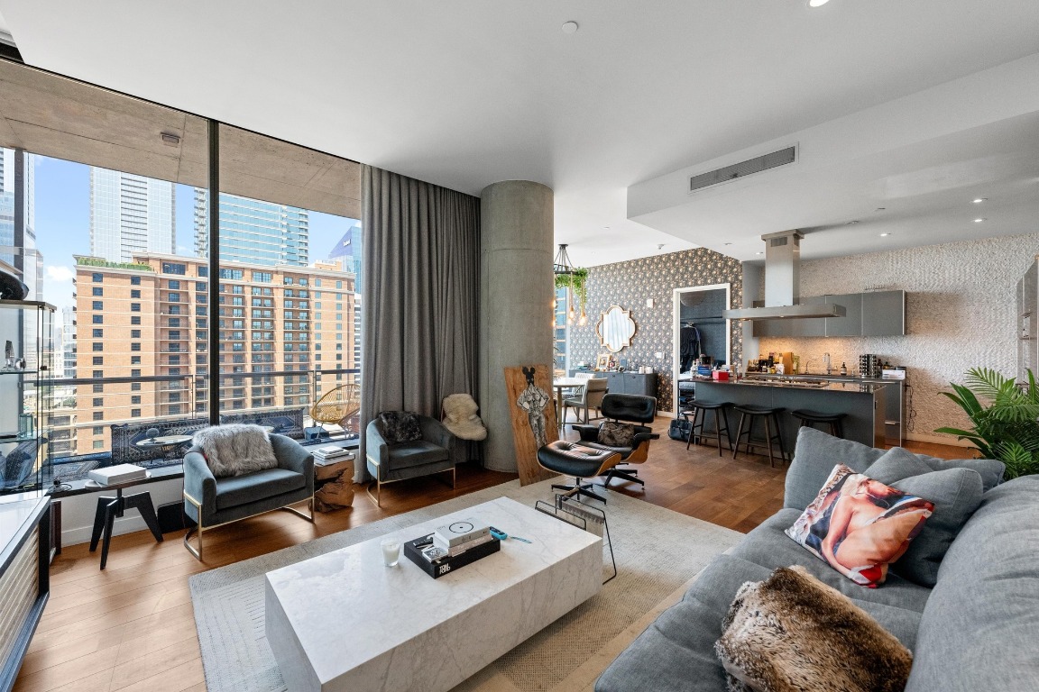 Expansive open-concept living area with floor-to-ceiling windows, wide-plank wood flooring, and seamless flow into the chef’s kitchen. Designer finishes, statement concrete column, and skyline views create a modern yet inviting space ideal for entertaining.