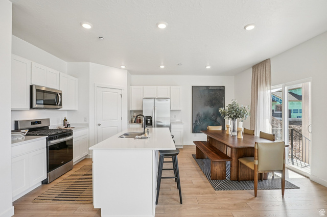 2097 North Ostler Peak Road, Unit 115 Heber City, UT 84032 - Photo 28 of 33 White kitchen cabinetry with stainless steel appliances and a center island, light wood-finish flooring, recessed lighting, and a sliding glass door