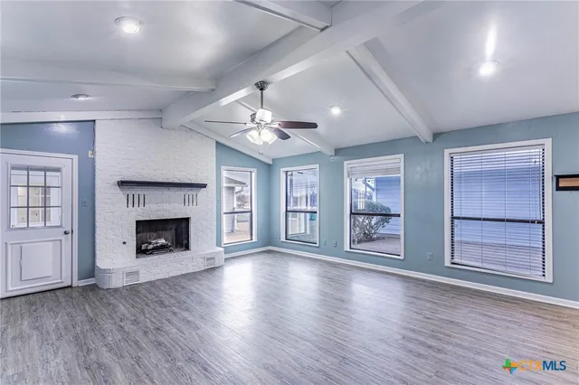a view of an empty room with wooden floor fireplace and a window