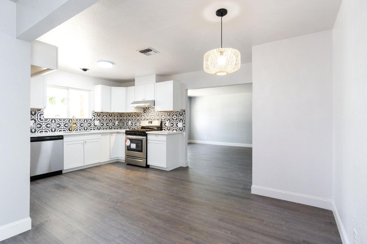 3086 West Hampton Way Fresno, CA 93722 - Photo 15 of 33 a large kitchen with granite countertop a stove a sink and white cabinets with wooden floor