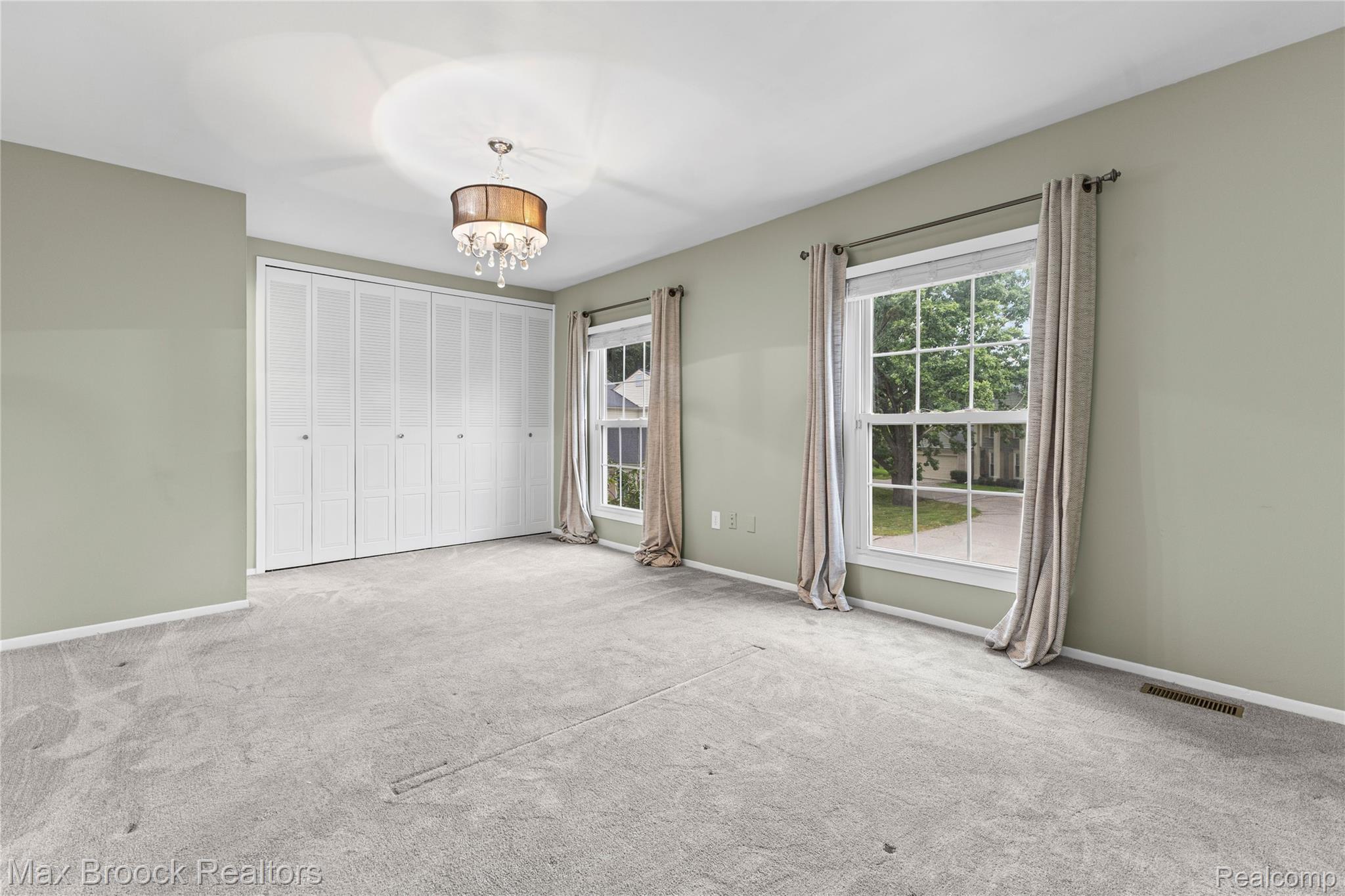 1157 Pine Ridge Court Rochester, MI 48306 - Photo 29 of 55 Spacious primary bedroom featuring neutral wall finishes, plush carpet flooring, a walk-in closet with bi-fold doors, dual windows with custom drapery hardware, and a ceiling-mounted light fixture with decorative drum shade