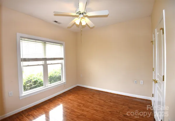 an empty room with wooden floor fan and windows