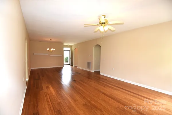 a view of an empty room with wooden floor and a fan