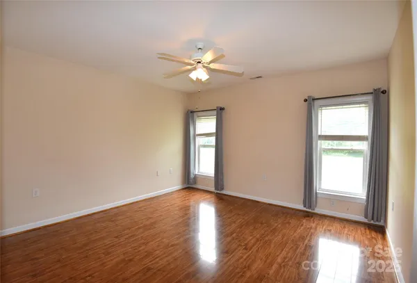 an empty room with wooden floor fan and windows