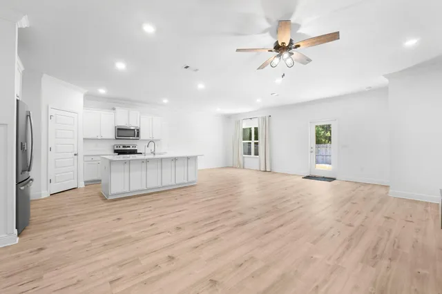 a view of an empty room with kitchen appliances and a ceiling fan