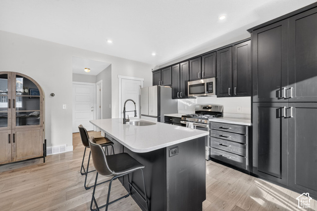 1081 Bowery Way Mapleton, UT 84664 - Photo 8 of 41 Kitchen featuring dark cabinetry, stainless steel appliances, a center island with sink, light-toned wood-finish flooring, and light countertops