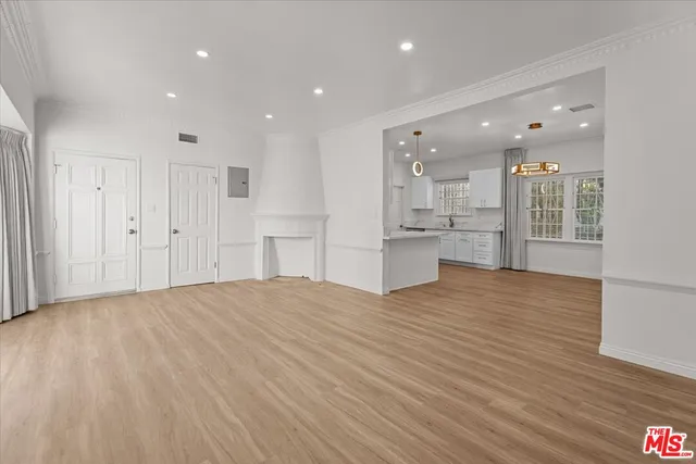 a view of an empty room with kitchen and window
