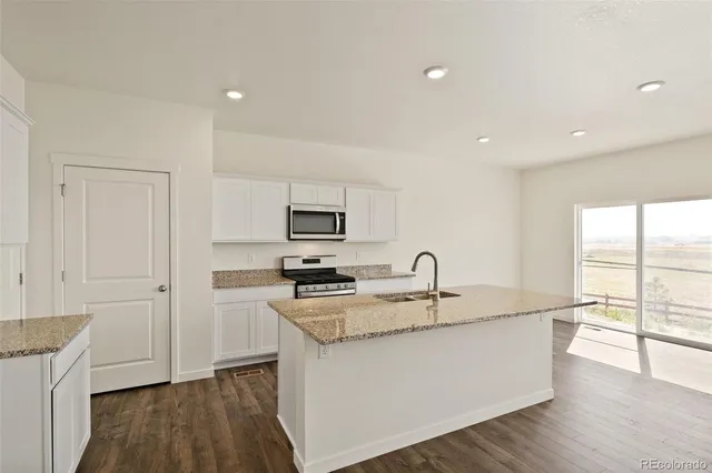 a kitchen with stainless steel appliances granite countertop a sink a stove and white cabinets with wooden floor