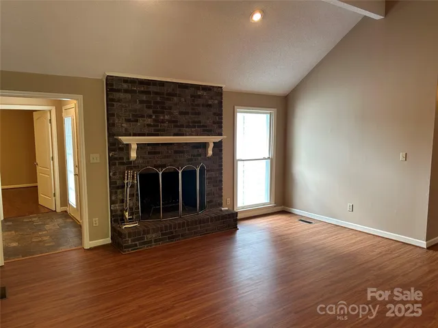 an empty room with wooden floor fireplace and windows