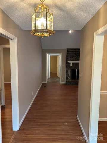 a view of a hallway to a room with wooden floor and chandelier