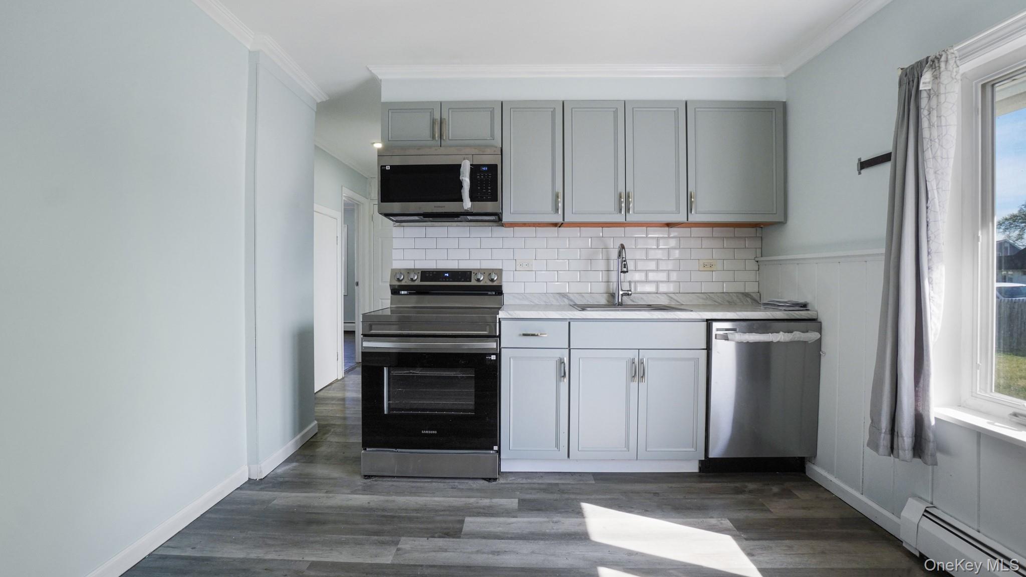 63 Blacksmith Road Levittown, NY 11756 - Photo 13 of 25 Kitchen area featuring light gray cabinetry, stainless steel appliances, a white subway tile backsplash, light-toned countertops, and wood-finish flooring
