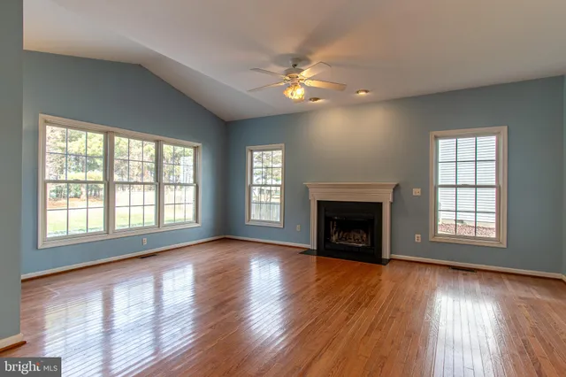 a view of an empty room with wooden floor fireplace and a window