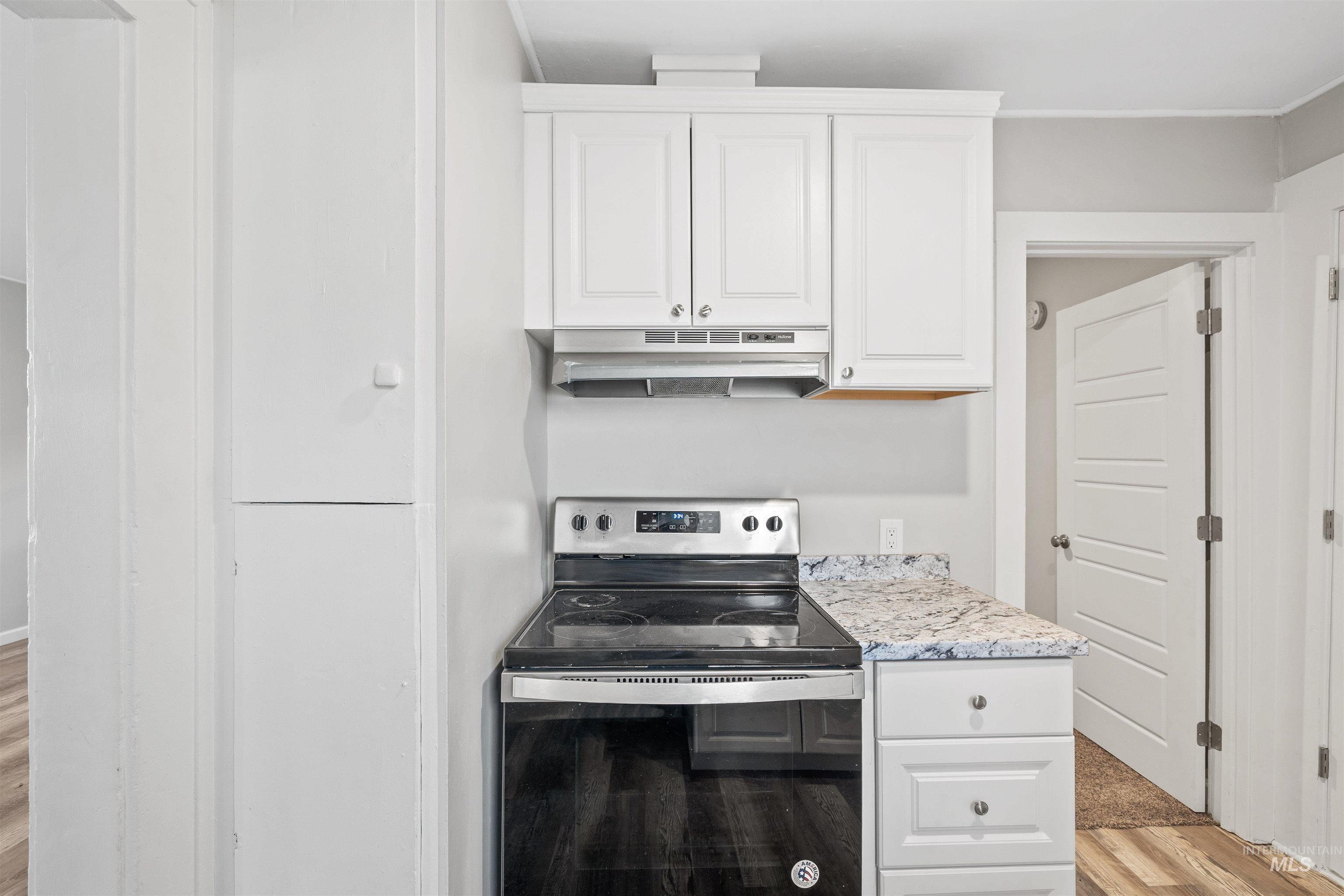 617 Eden Street North Twin Falls, ID 83301 - Photo 10 of 25 Kitchen with electric range, white cabinets, under cabinet range hood, and light wood-style flooring
