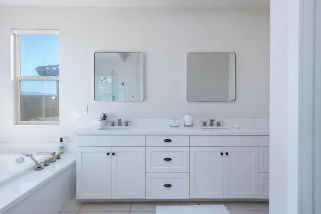 a bathroom with white cabinets a sink a window and mirror