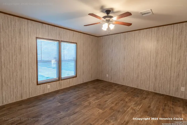 an empty room with wooden floor chandelier fan and windows