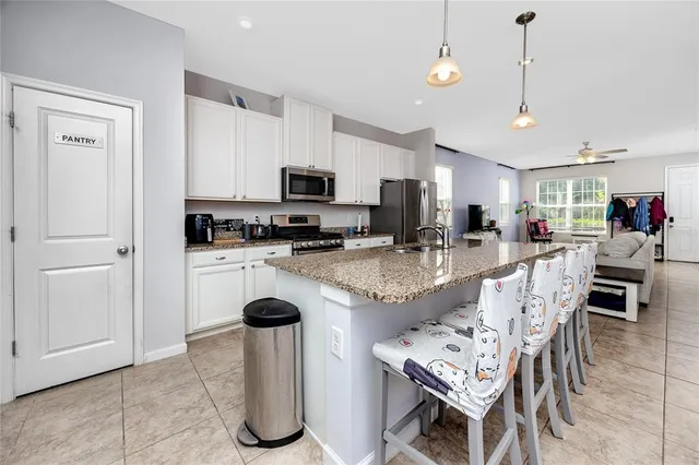 a kitchen with stainless steel appliances granite countertop a stove top oven a refrigerator a sink a dining table and chairs with white cabinets