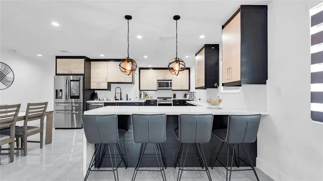 a kitchen with stainless steel appliances a stove a sink a microwave a refrigerator a center island and chairs