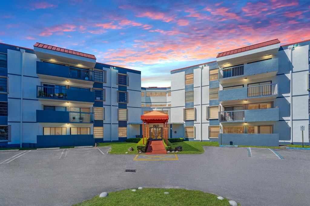 a front view of a building with a garden and parking