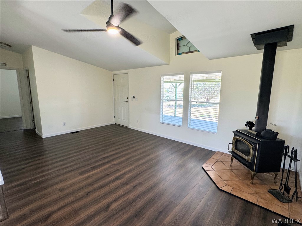 1575 South Roy Road Kingman, AZ 86401 - Photo 34 of 56 Living area featuring wood-look flooring, a ceiling fan, a wood-burning stove with a tiled hearth, and windows providing outdoor views