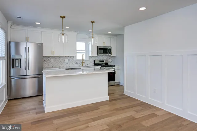 a kitchen with stainless steel appliances granite countertop a refrigerator a sink a stove a microwave and white cabinets with wooden floor