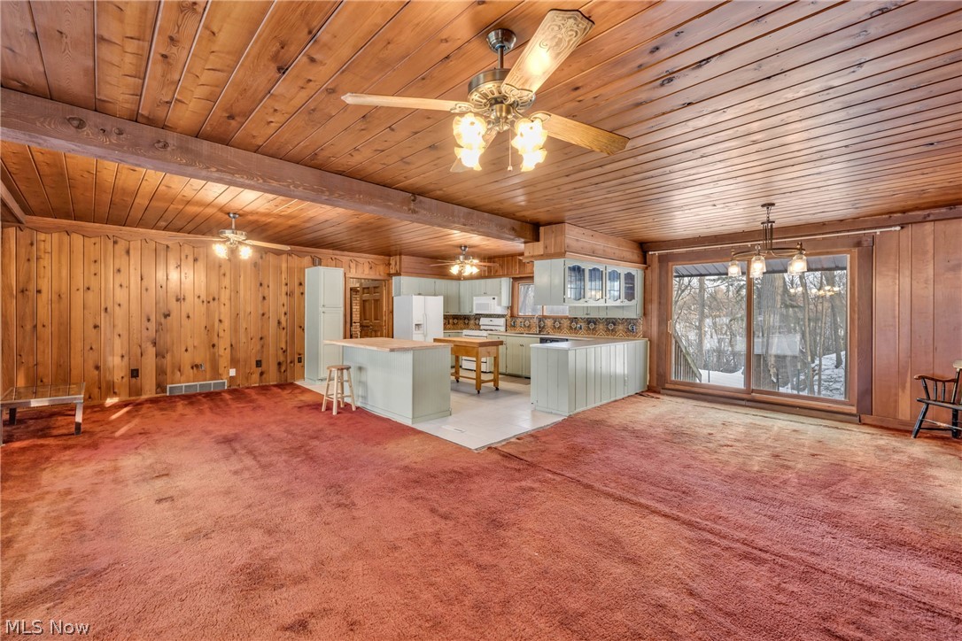 22791 Harms Road Euclid, OH 44143 - Photo 7 of 39 Unfurnished living room with wooden walls, light carpet, a wooden ceiling with exposed beams, and a ceiling fan