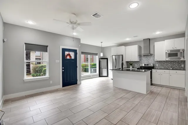 a large white kitchen with granite countertop a stove a sink a refrigerator and white cabinets with wooden floor