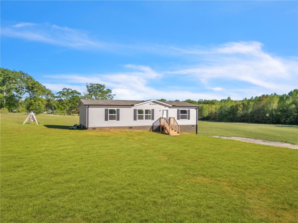 This property features a charming home nestled on a spacious green lawn, surrounded by natural beauty.