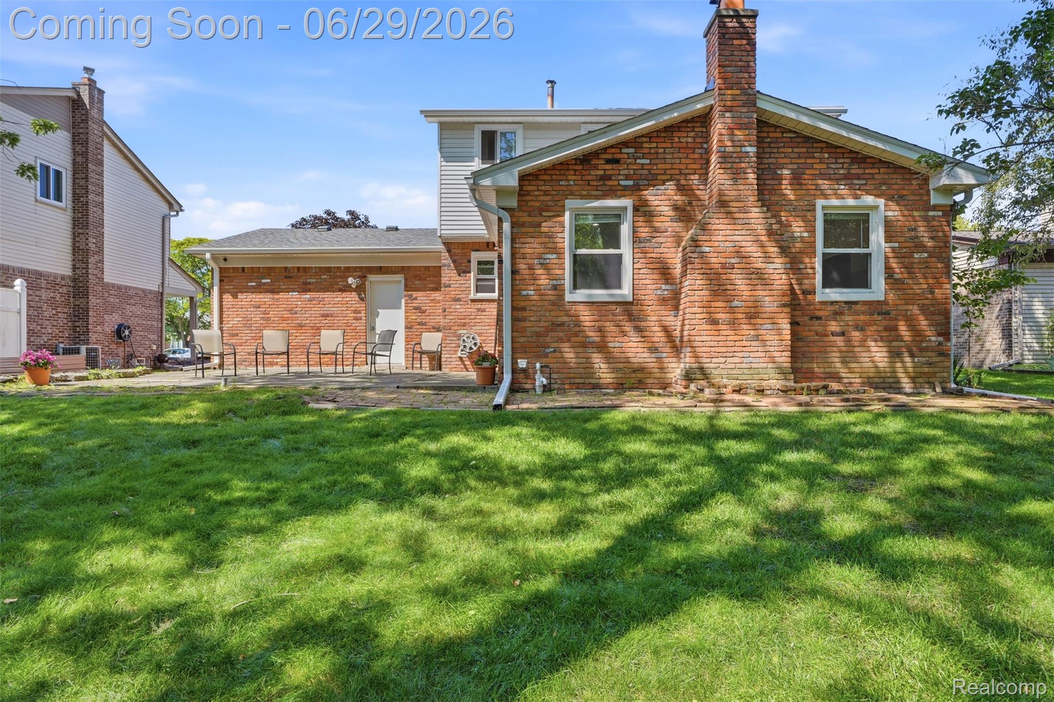 45179 Rudgate Road Canton, MI 48188 - Photo 30 of 48 Expansive grassy yard with a brick exterior featuring white-framed windows, a brick chimney, and a paved patio area