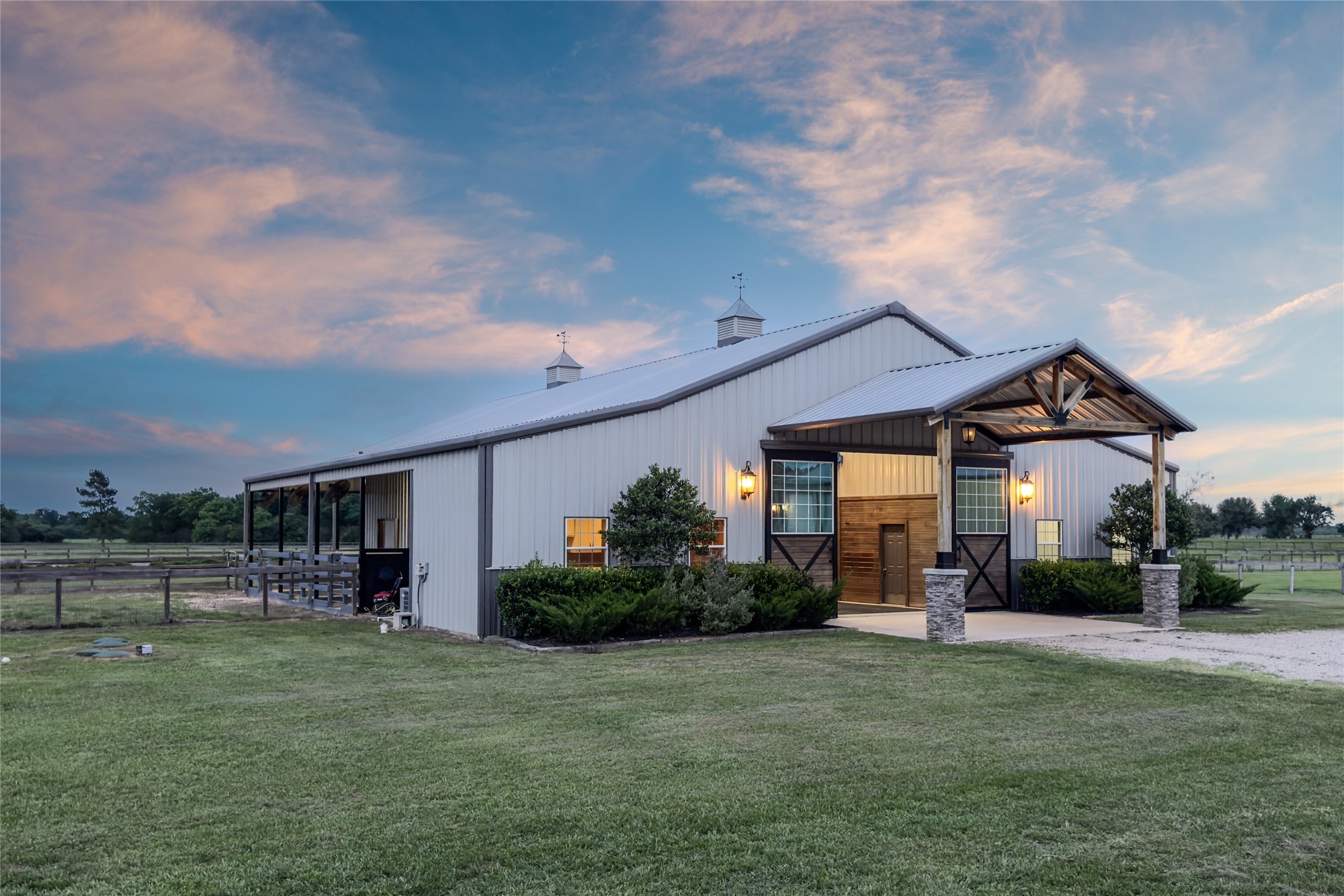 24118 Margerstadt Road Hockley, TX 77447 - Photo 35 of 46 Warm lighting, custom stall fronts, and open breezeways give the equestrian facilities a clean and refined feel as evening settles across the property. The layout balances everyday practicality with the calmer atmosphere that defines Paloma Ridge Farm.