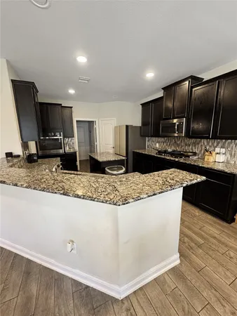 a kitchen with kitchen island granite countertop a sink a stove a refrigerator cabinets and a dining table