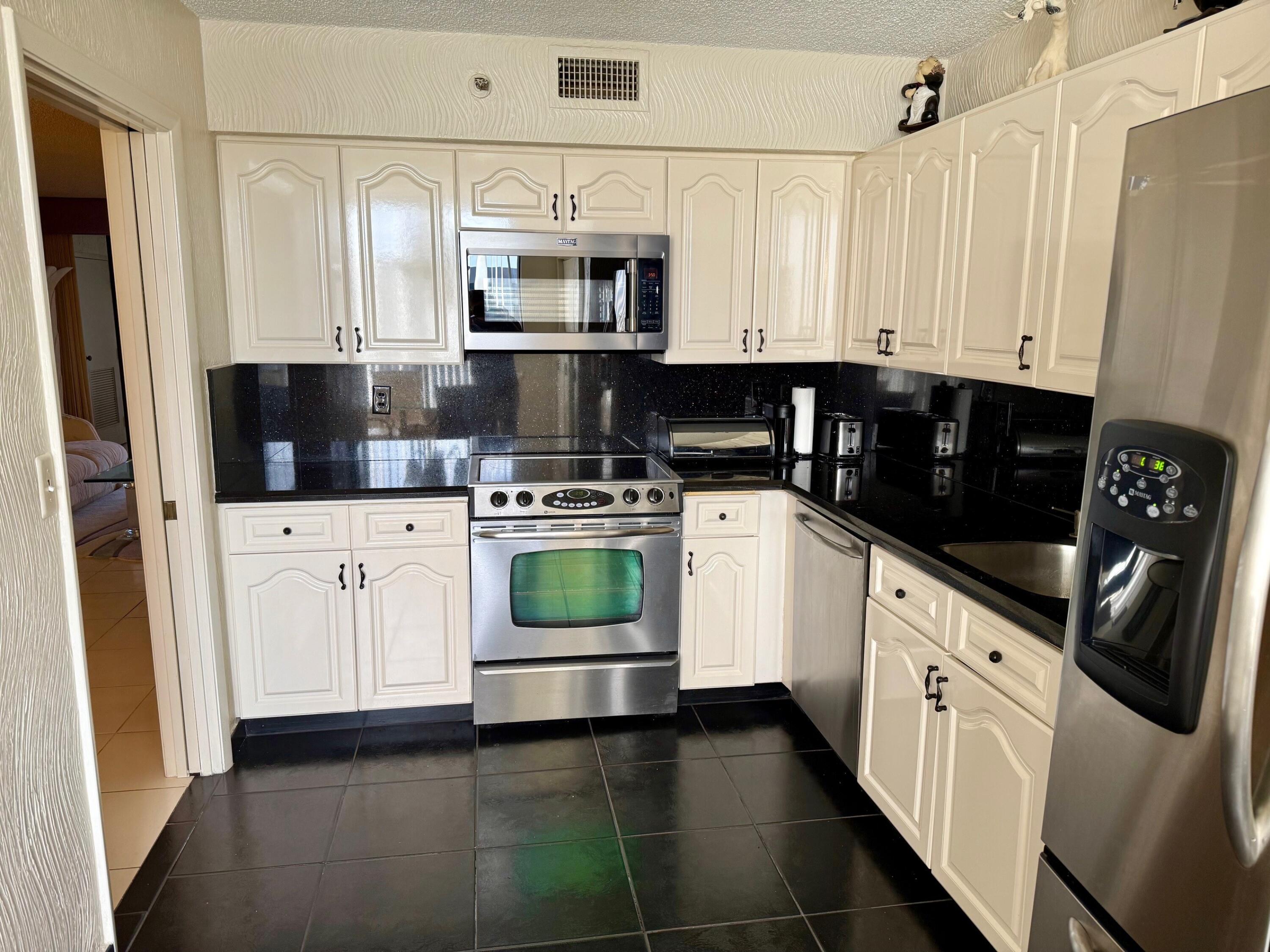 7564 Regency Lake Drive, Unit 702 Boca Raton, FL 33433 - Photo 2 of 40 a kitchen with white cabinets and white appliances