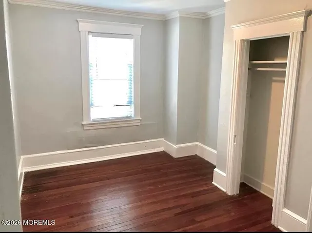 an empty room with wooden floor closet and windows