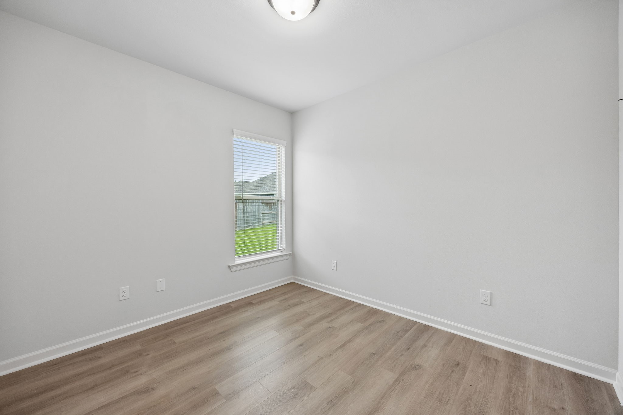 10902 Bonfire Trail Beasley, TX 77417 - Photo 22 of 36 This is a bright, empty secondary bedroom with light-color walls and wood flooring. It features a window with blinds overlooking a grassy yard, providing natural light. Ideal for a small bedroom or office space.